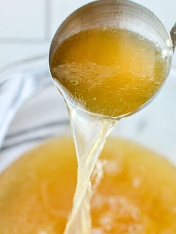 A bowl of chicken broth, with a ladle adding more chicken broth to the bowl.