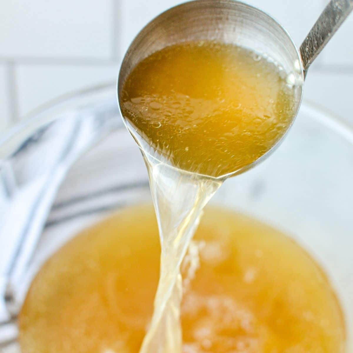 A bowl of chicken broth, with a ladle adding more chicken broth to the bowl.