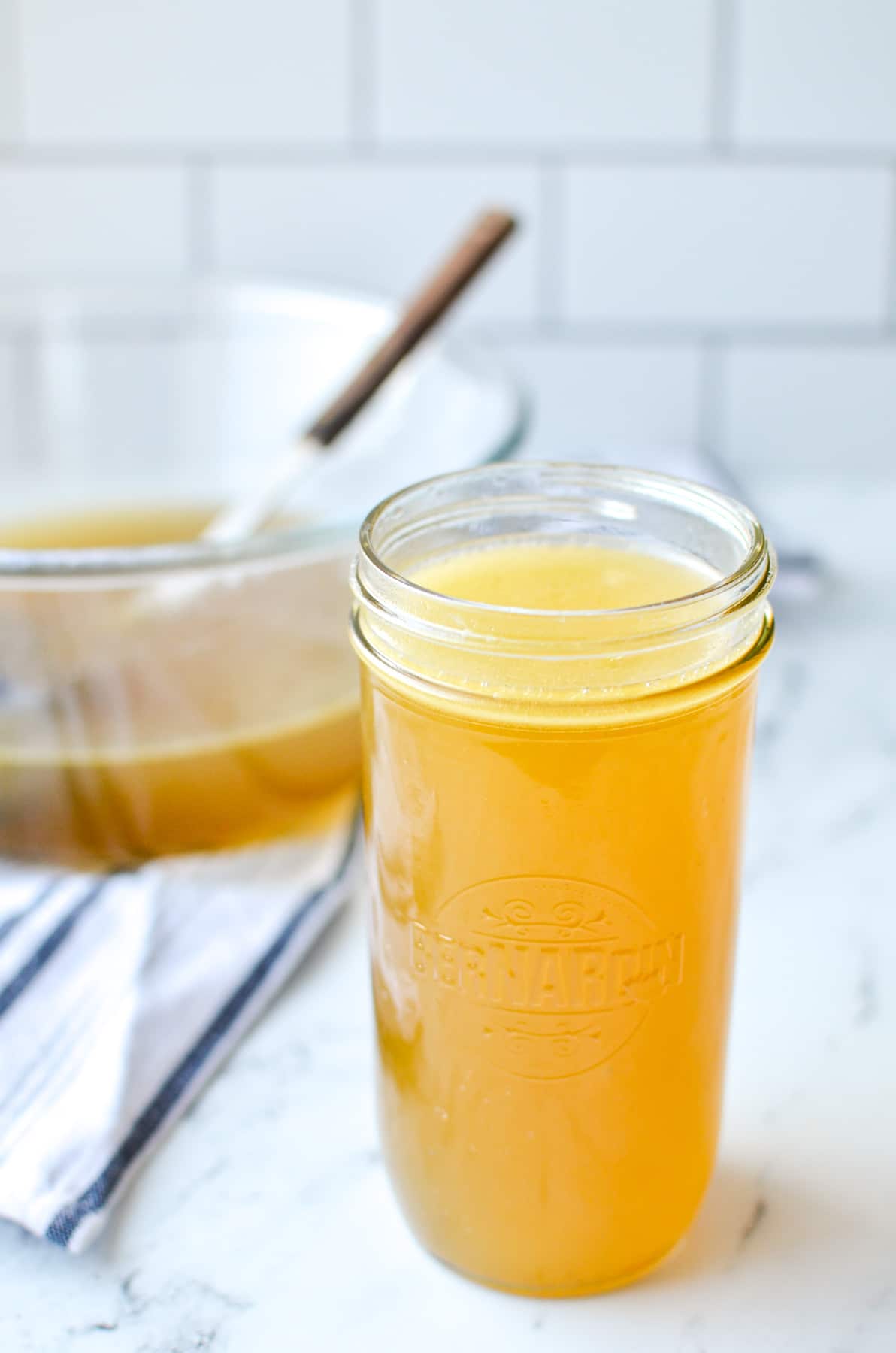 A jar of homemade chicken broth with a large bowl in the background