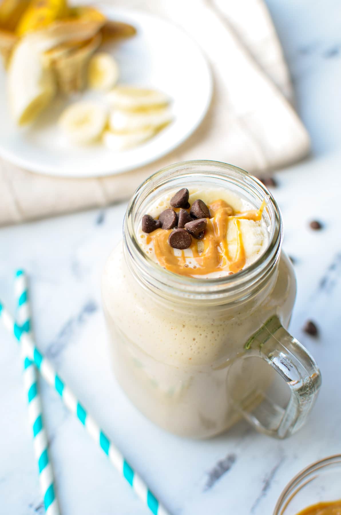 A glass with a peanut butter and banana kefir smoothie. Drizzled with peanut butter and topped with chocolate chips.