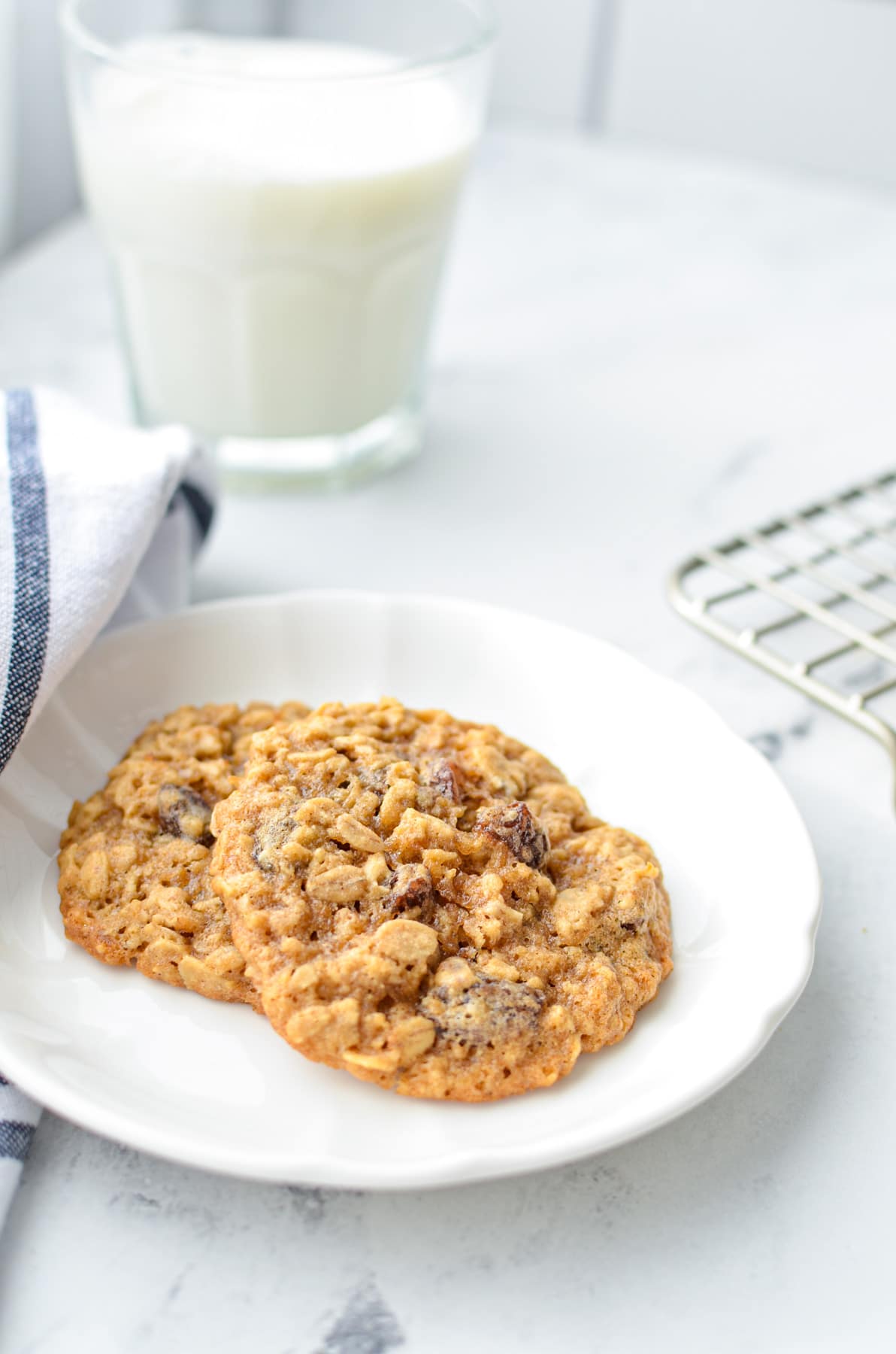 Two sourdough oatmeal raisin cookies on a plate with a glass of milk in the background.