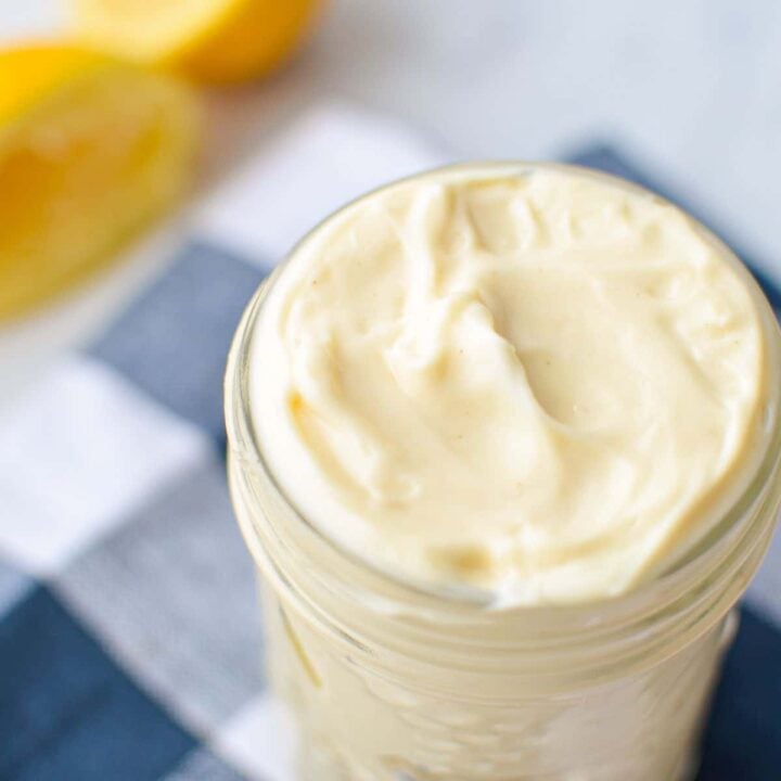 A small jar of homemade avocado oil mayo, with some lemons in the background.