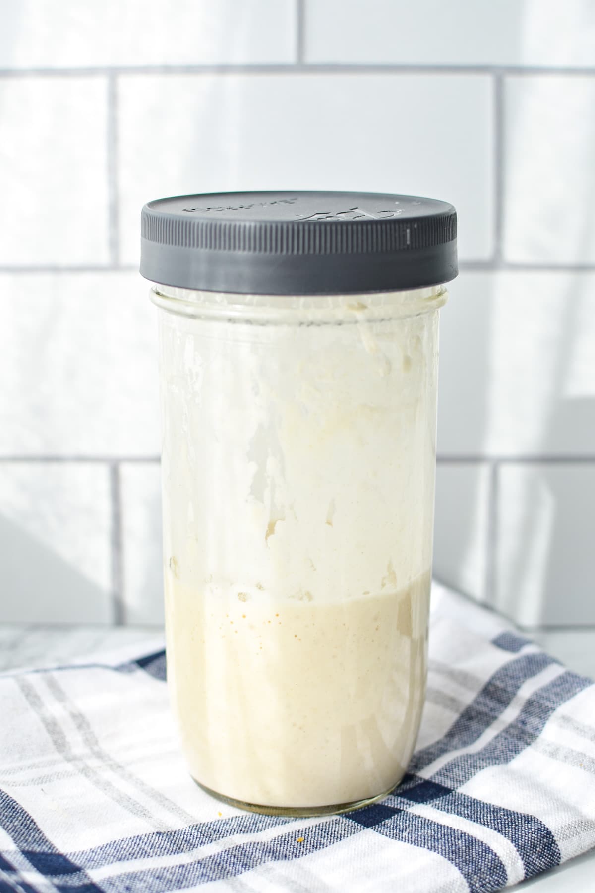 A jar of sourdough starter, resting on a blue striped napkin.