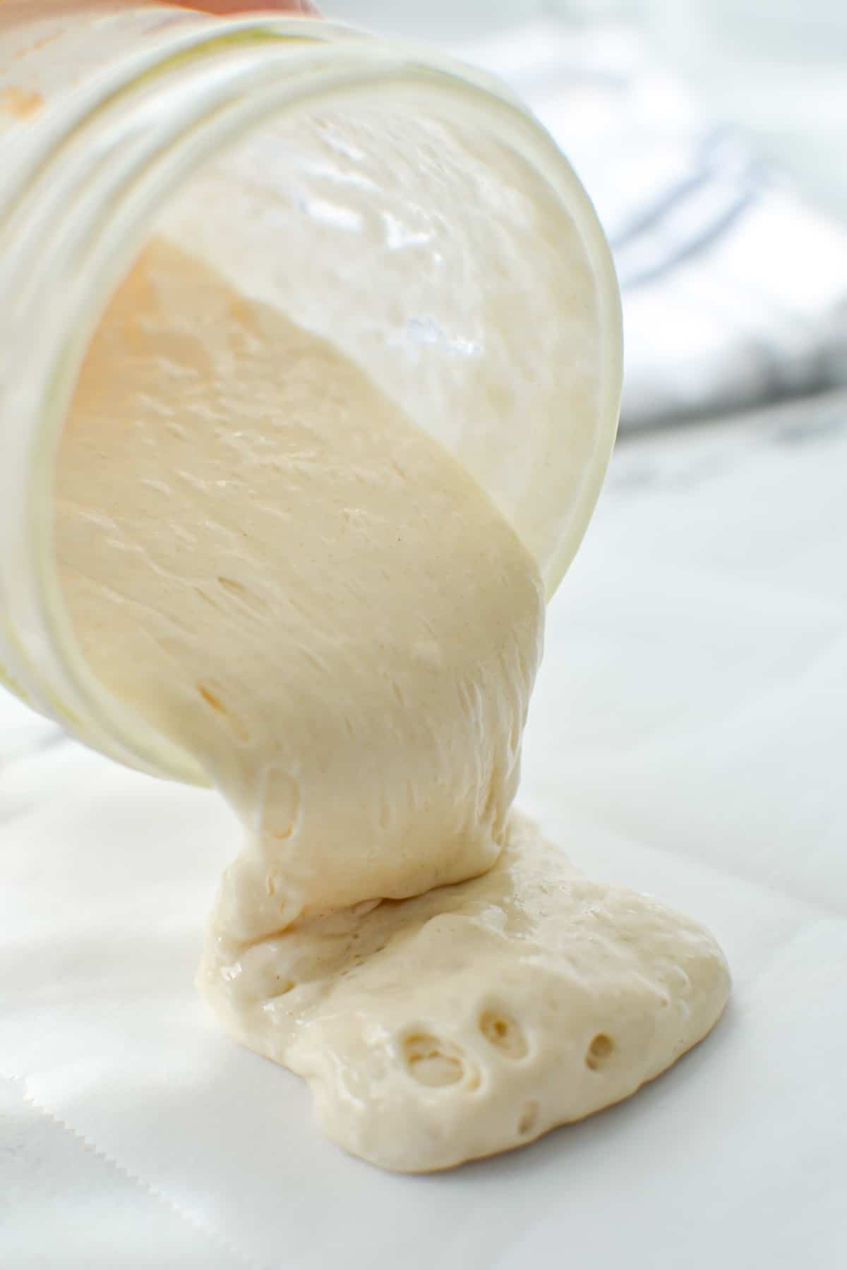 Pouring sourdough starter onto a piece of parchment paper.