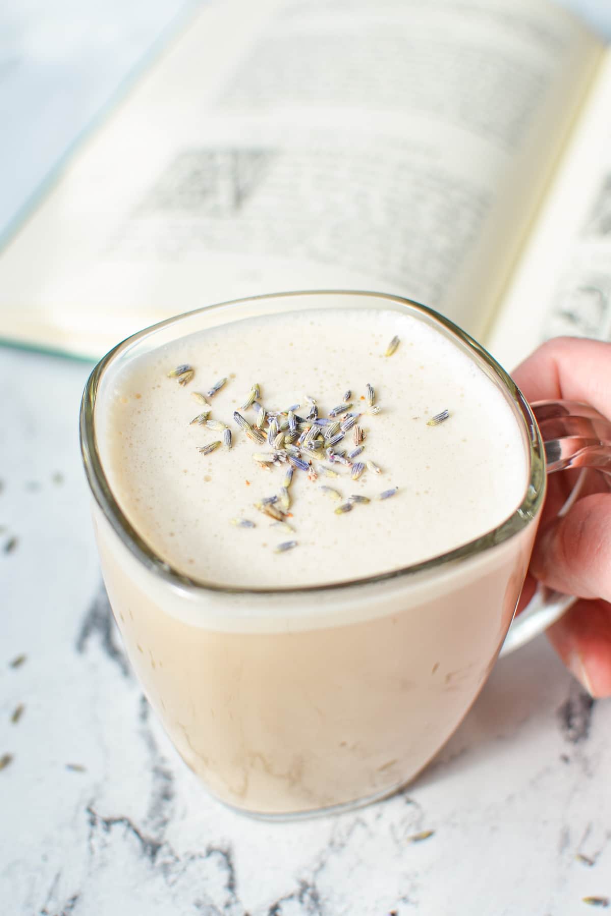 A hand holding a mug of a tea latte, with a book in the background.