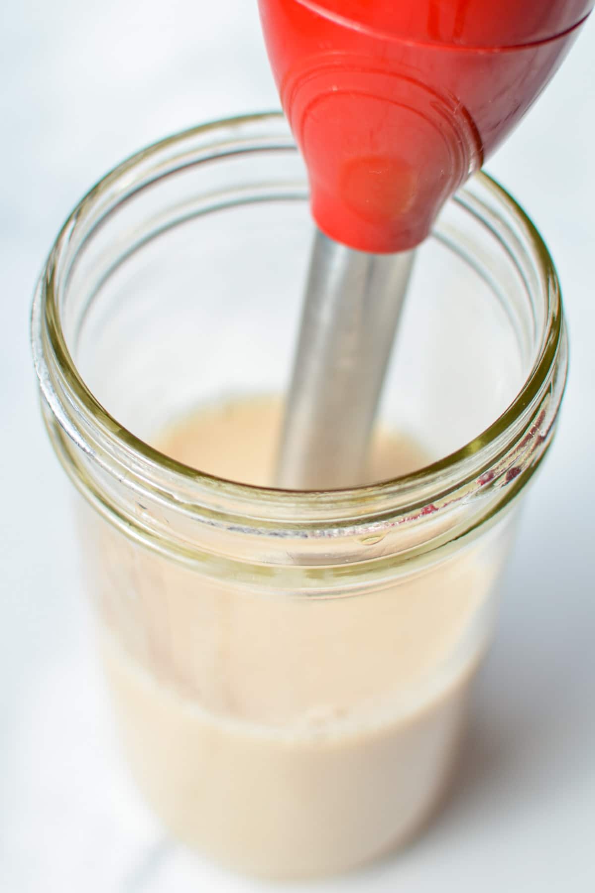 Adding an immersion blender to a jar of tea and milk.