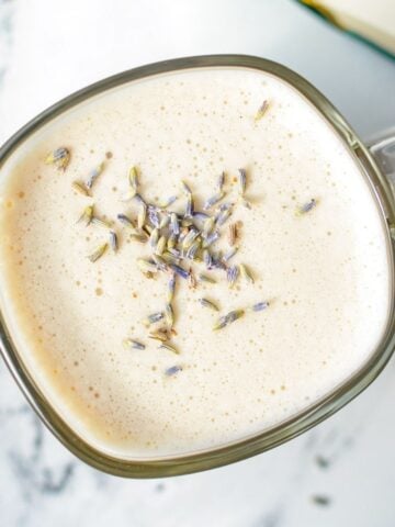 A glass mug of a London Fog Latte, with dried lavender buds.