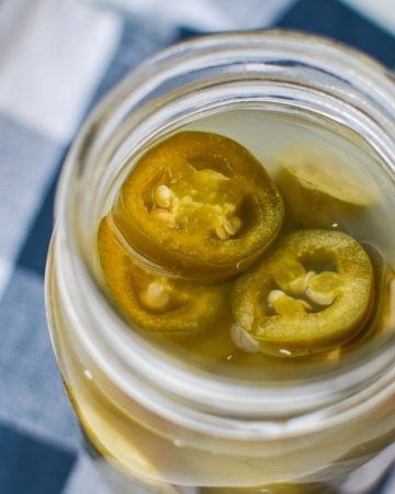 A jar of fermented jalapeno peppers, resting on a blue check napkin.
