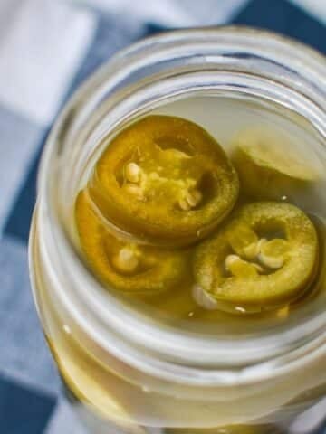 A jar of fermented jalapeno peppers, resting on a blue check napkin.