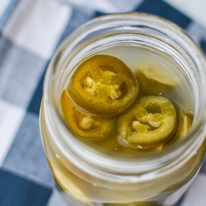 A jar of fermented jalapeno peppers, resting on a blue check napkin.