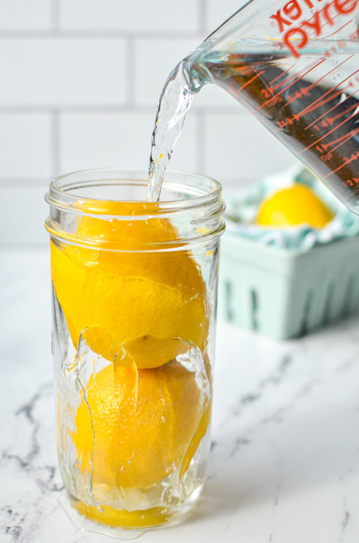 Pouring water into a mason jar with two lemons in it.