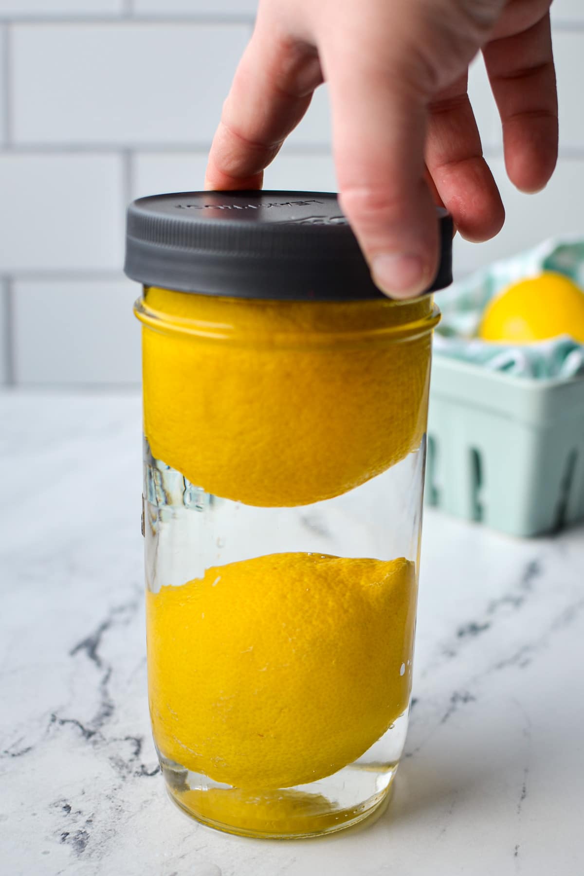 Adding a lid to a jar of lemons that have been covered in water.
