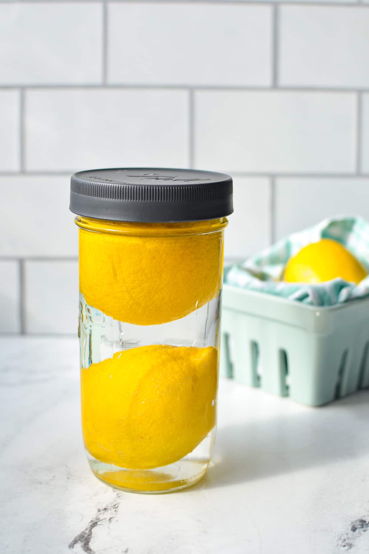 A jar with two lemons, filled with water and topped with a lid.
