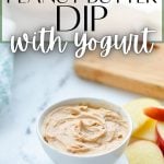 A small bowl of peanut butter dip, with a cutting board and apple slices in the background.