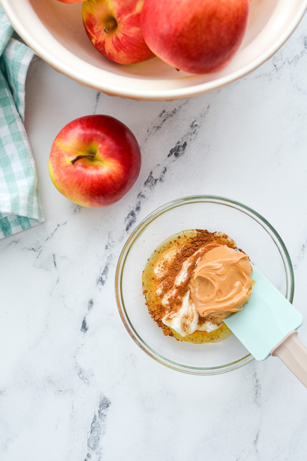 A small bowl filled with greek yogurt, peanut butter, honey, cinnamon and vanilla. A bowl of apples in the top left corner.