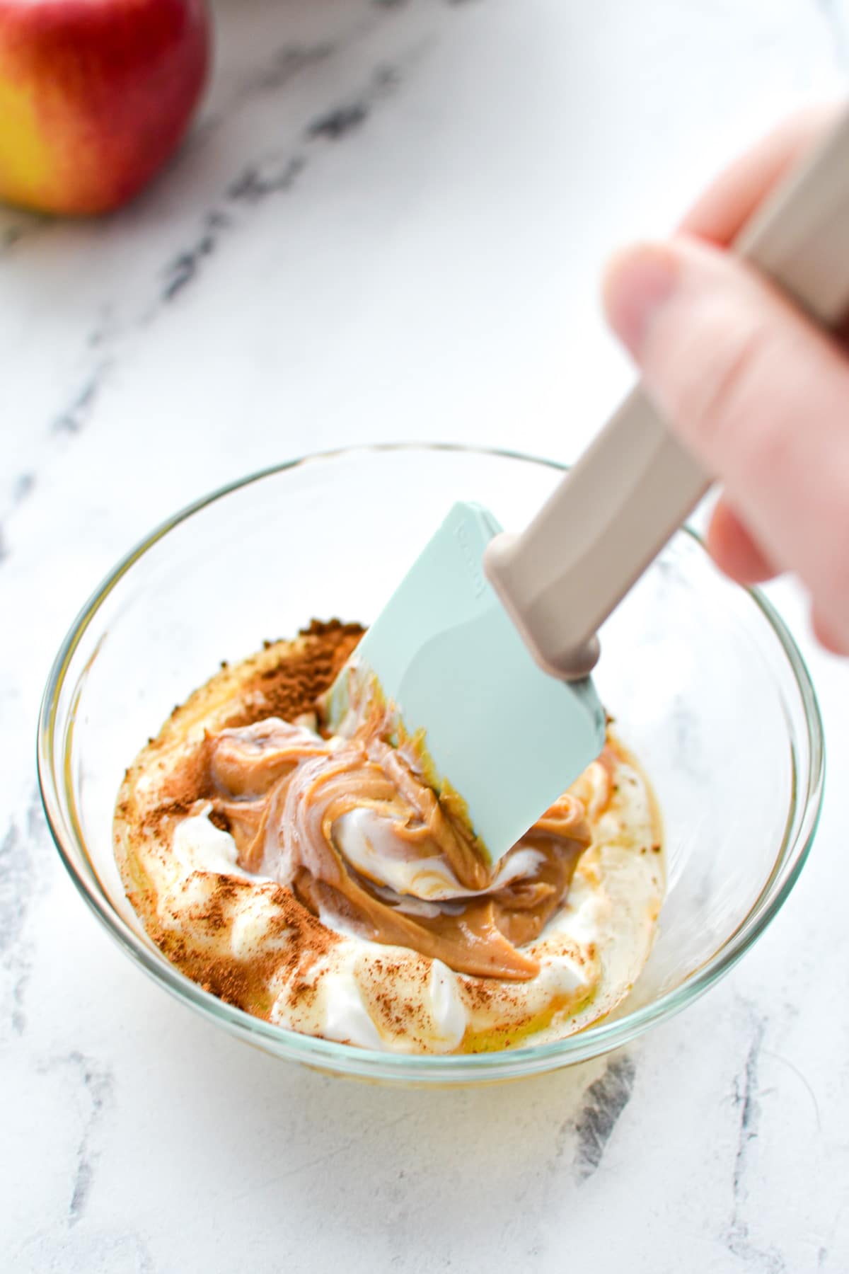 A silicone spatula stirring a small bowl of greek yogurt and peanut butter.