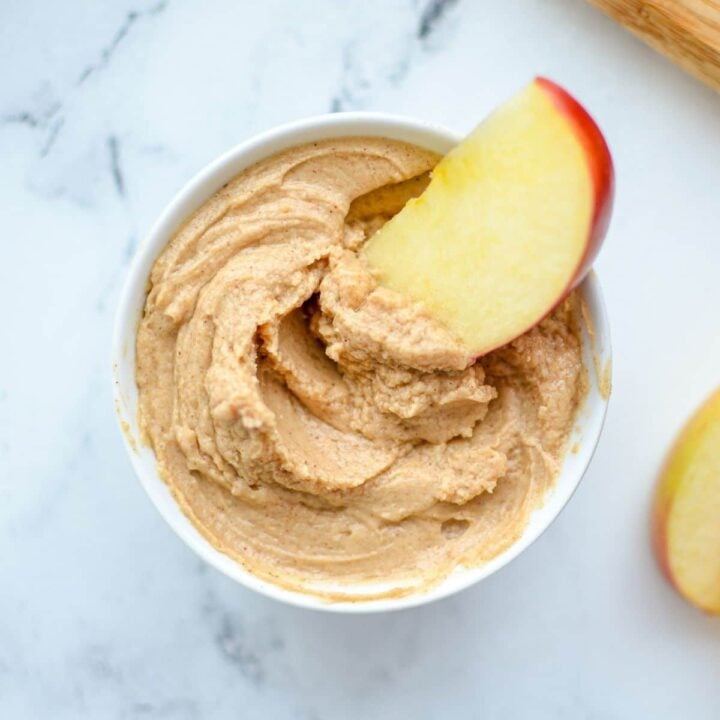 A small bowl of yogurt dip, with an apple slice sticking out.