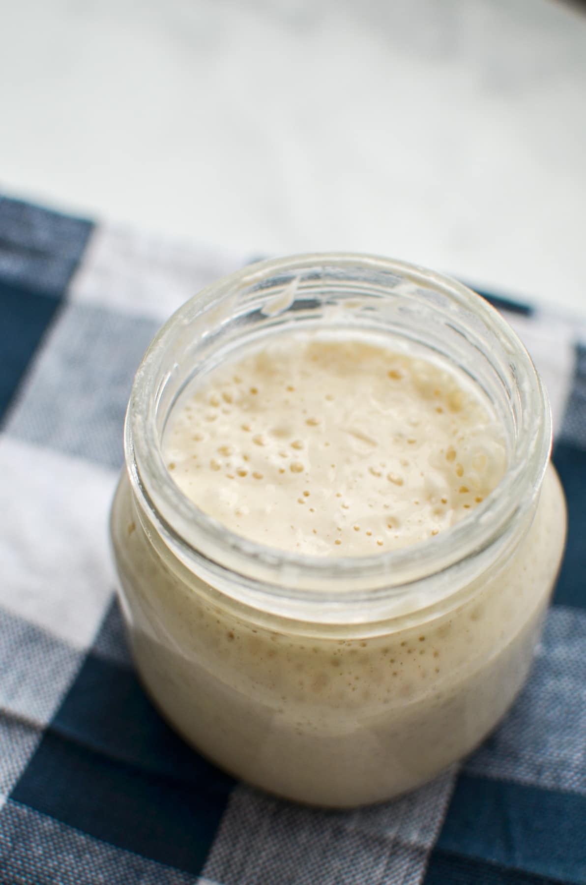 A jar of sourdough starter resting on a blue check napkin.