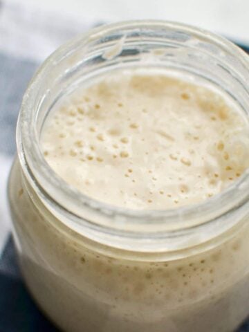 A jar of sourdough starter on a blue check napkin.