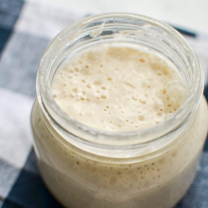 A jar of sourdough starter on a blue check napkin.