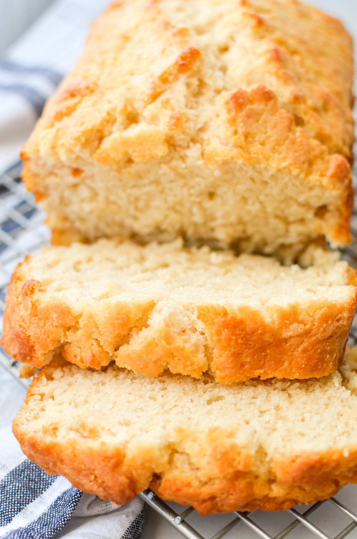 A loaf of beer bread, sliced and resting on a wire rack for cooling.