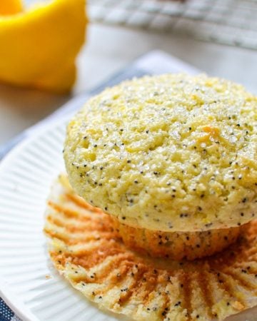 A close up of a lemon poppy seed muffin, with a lemon in the background.