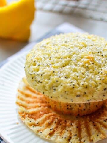 A close up of a lemon poppy seed muffin, with a lemon in the background.