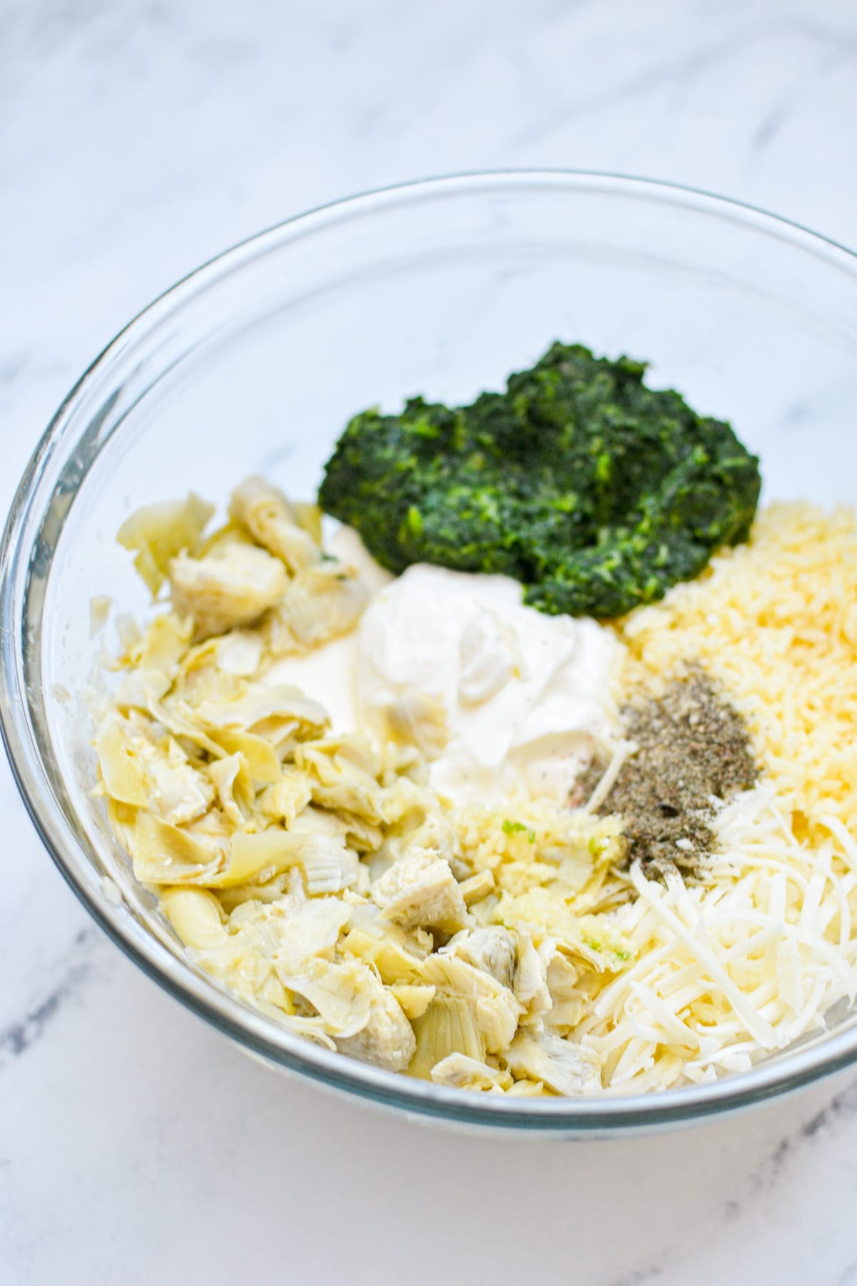 A bowl of ingredients needed to make spinach artichoke dip, not yet mixed together.