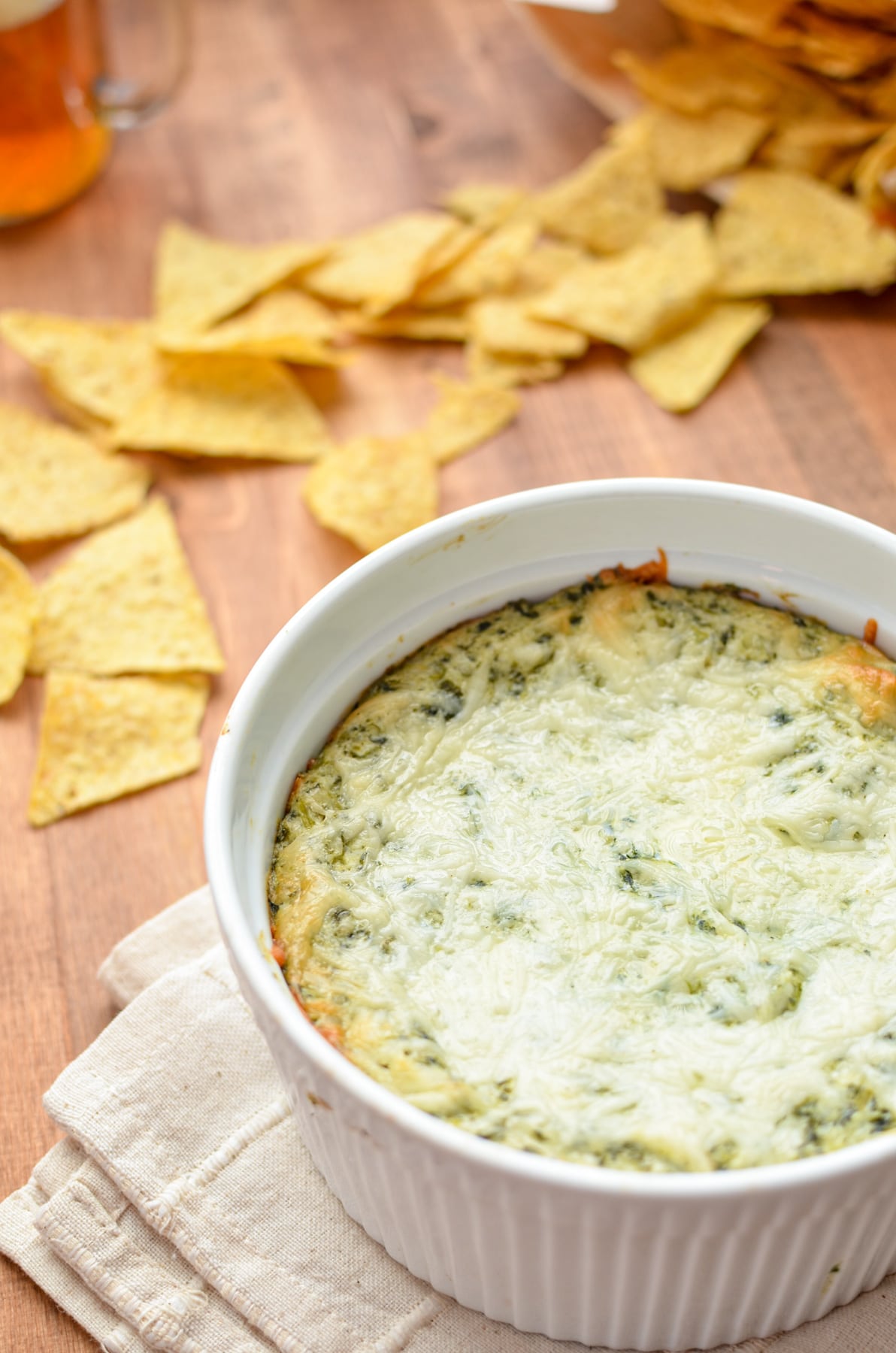 A 2 quart round dish filled with a baked spinach artichoke dip and surrounded by tortilla chips.