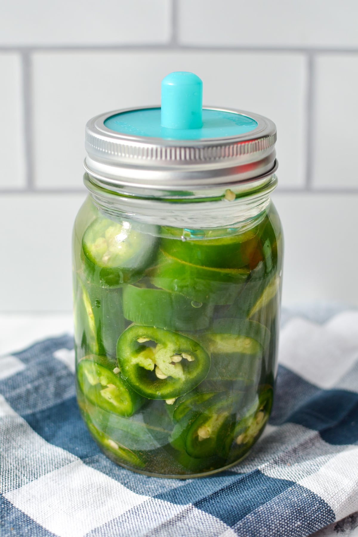 A jar of fermenting peppers with a fermentation lid on top.