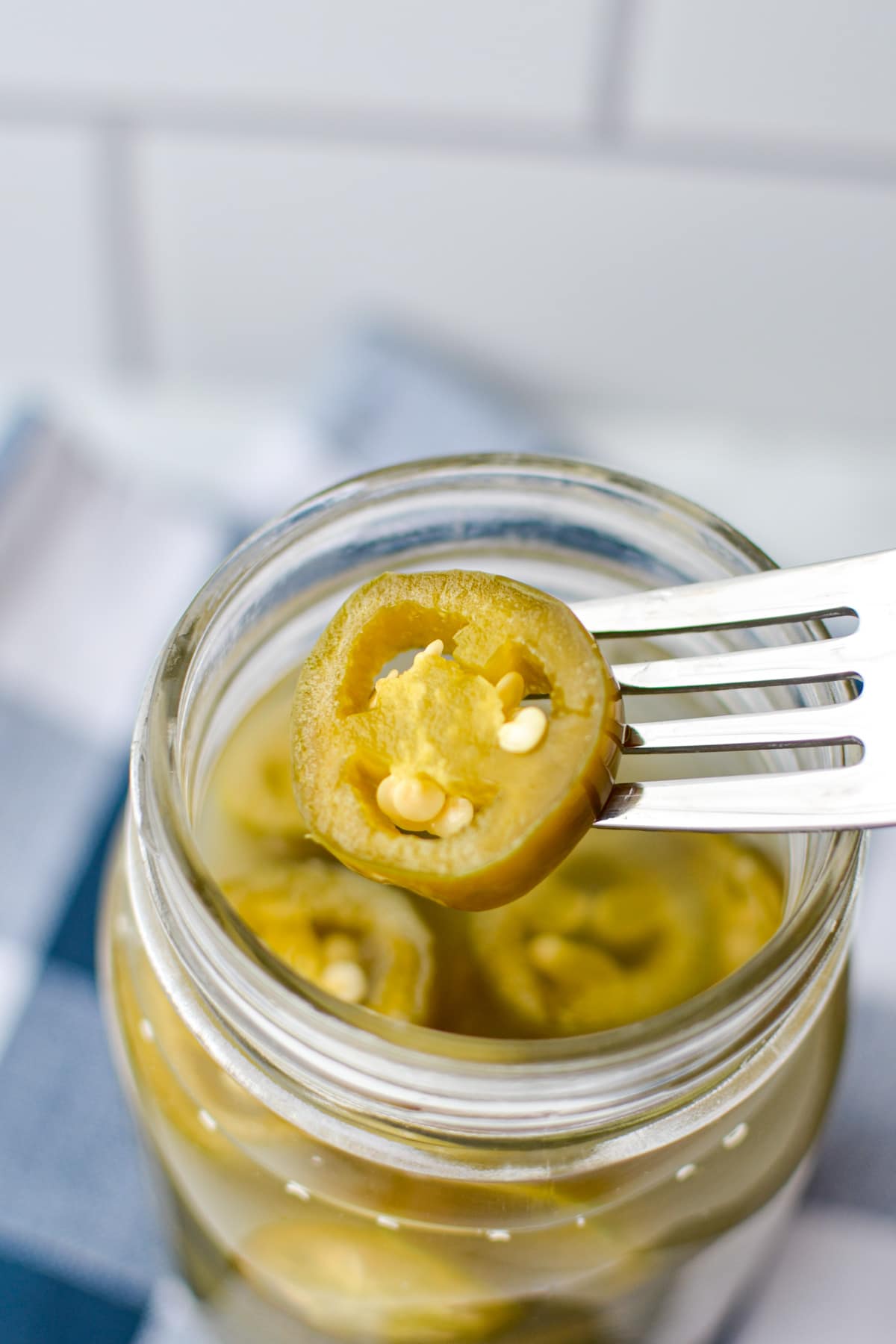 A fork reaching into a jar to pull out some fermented jalapeno slices.