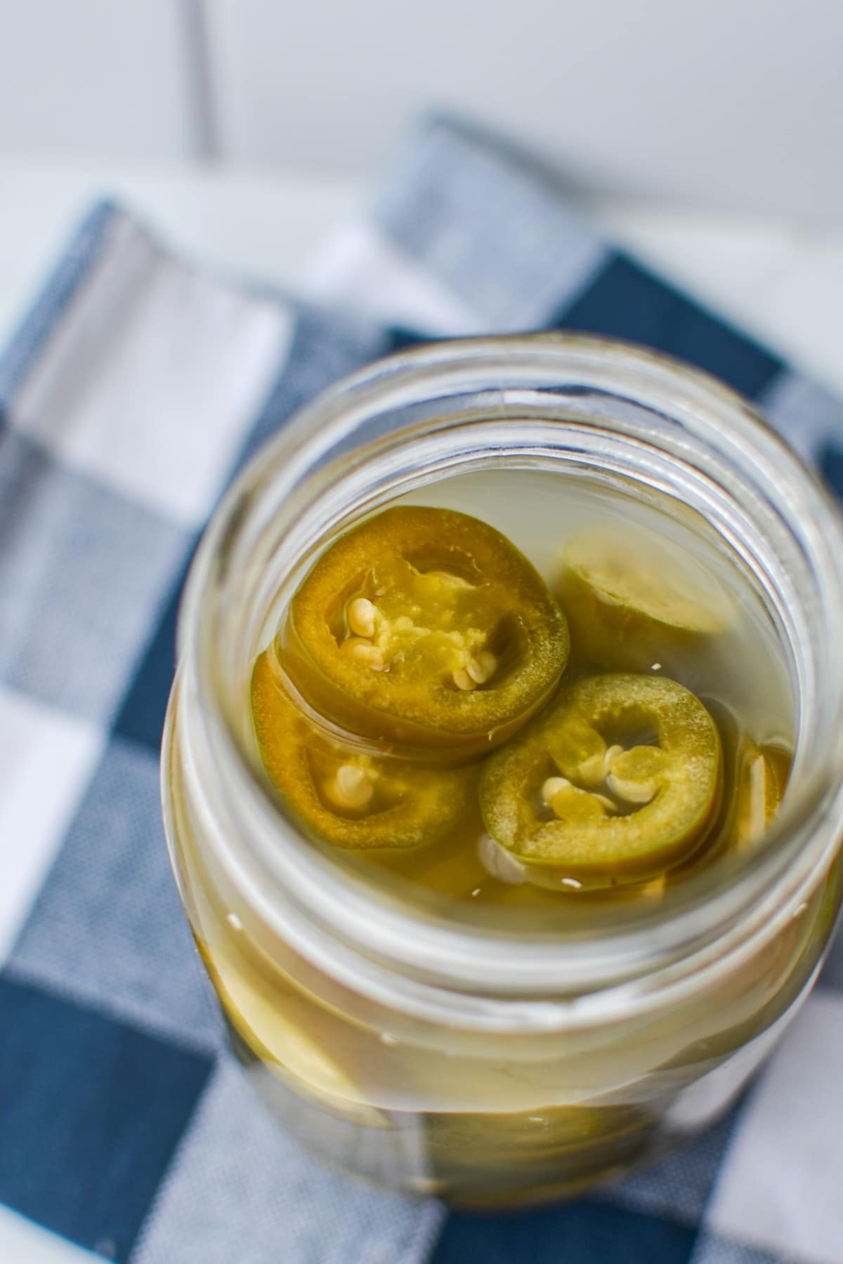 A jar of fermented jalapeno slices, on a blue check napkin.