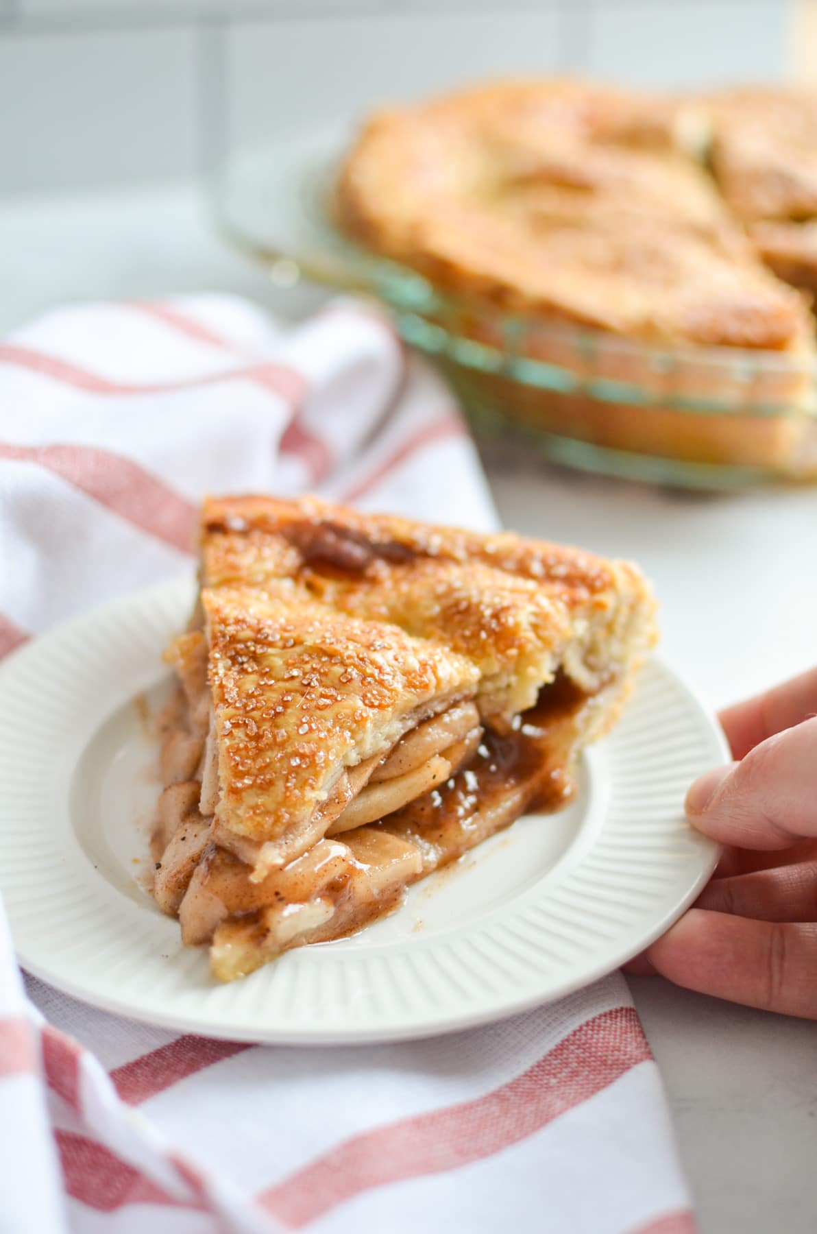 A hand holding a small plate of sourdough apple pie, resting on a white and red napkin.