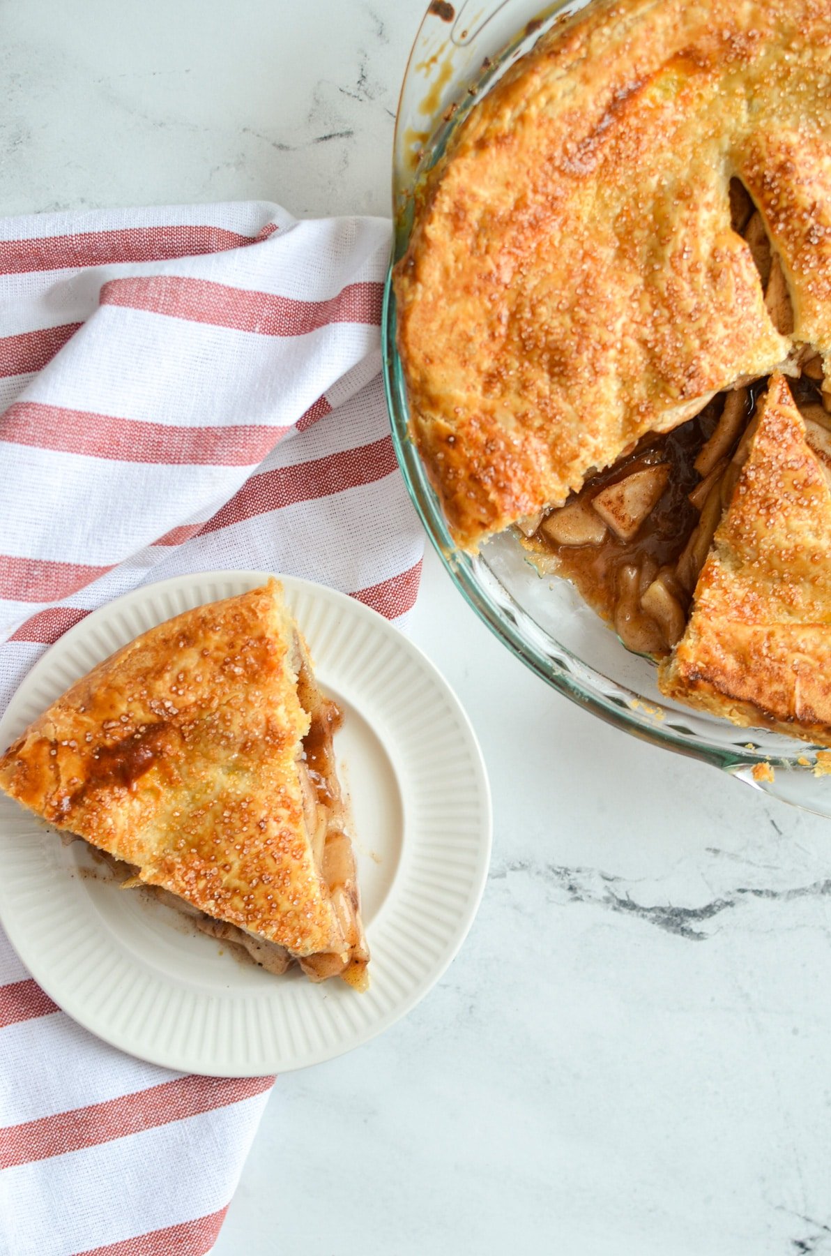 A slice of apple pie removed from the larger pie next to it.