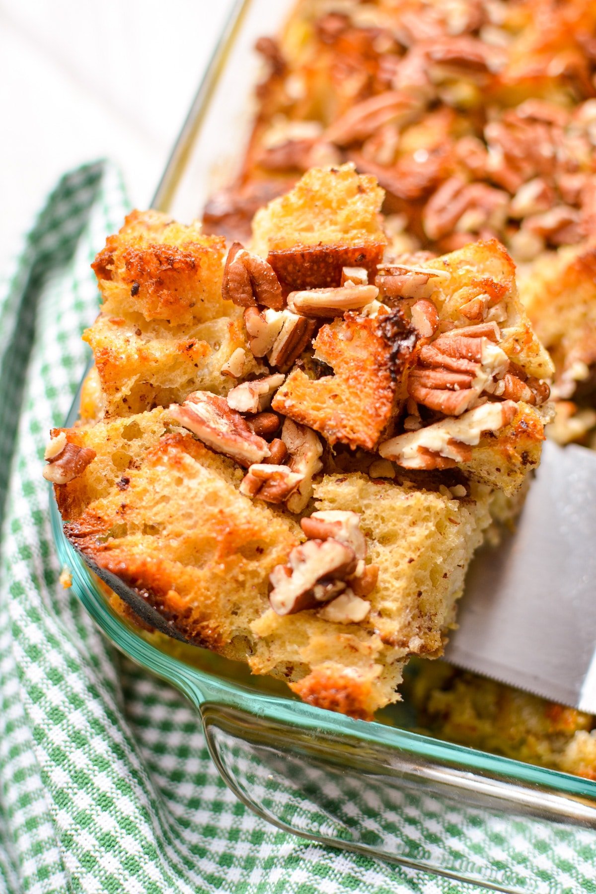 Lifting a slice of sourdough bread pudding from a baking dish.