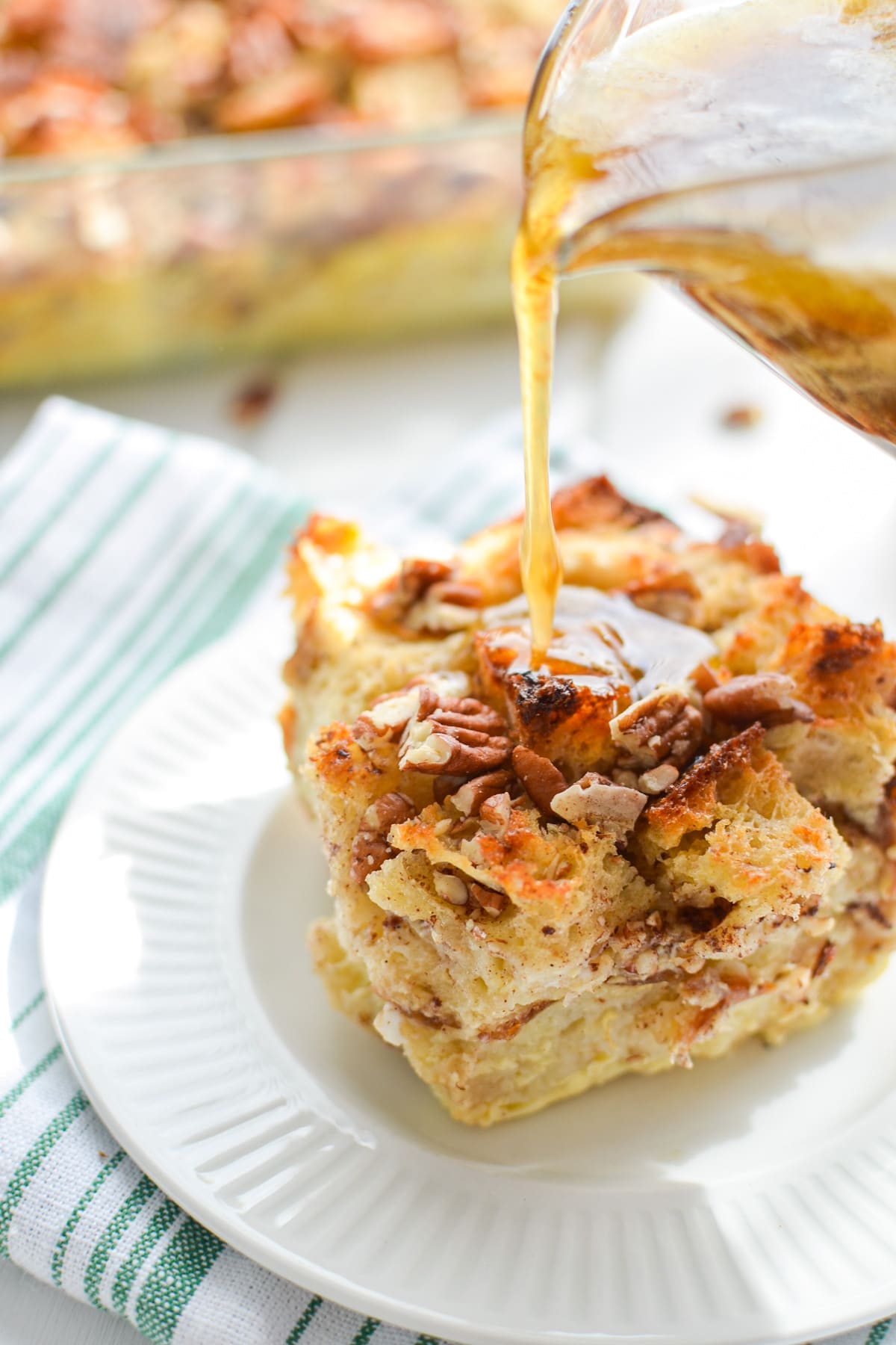 A close up of a slice of bread pudding, being drizzled with a brown sugar topping.