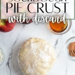 An overhead shot of a ball of pie dough wrapped in plastic wrap.