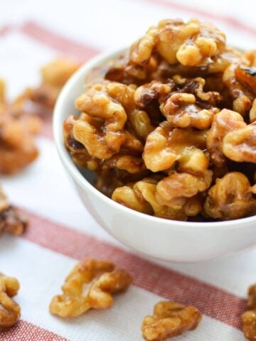 A small white bowl on a red and white striped napkin. Filled and overflowing with candied walnuts.