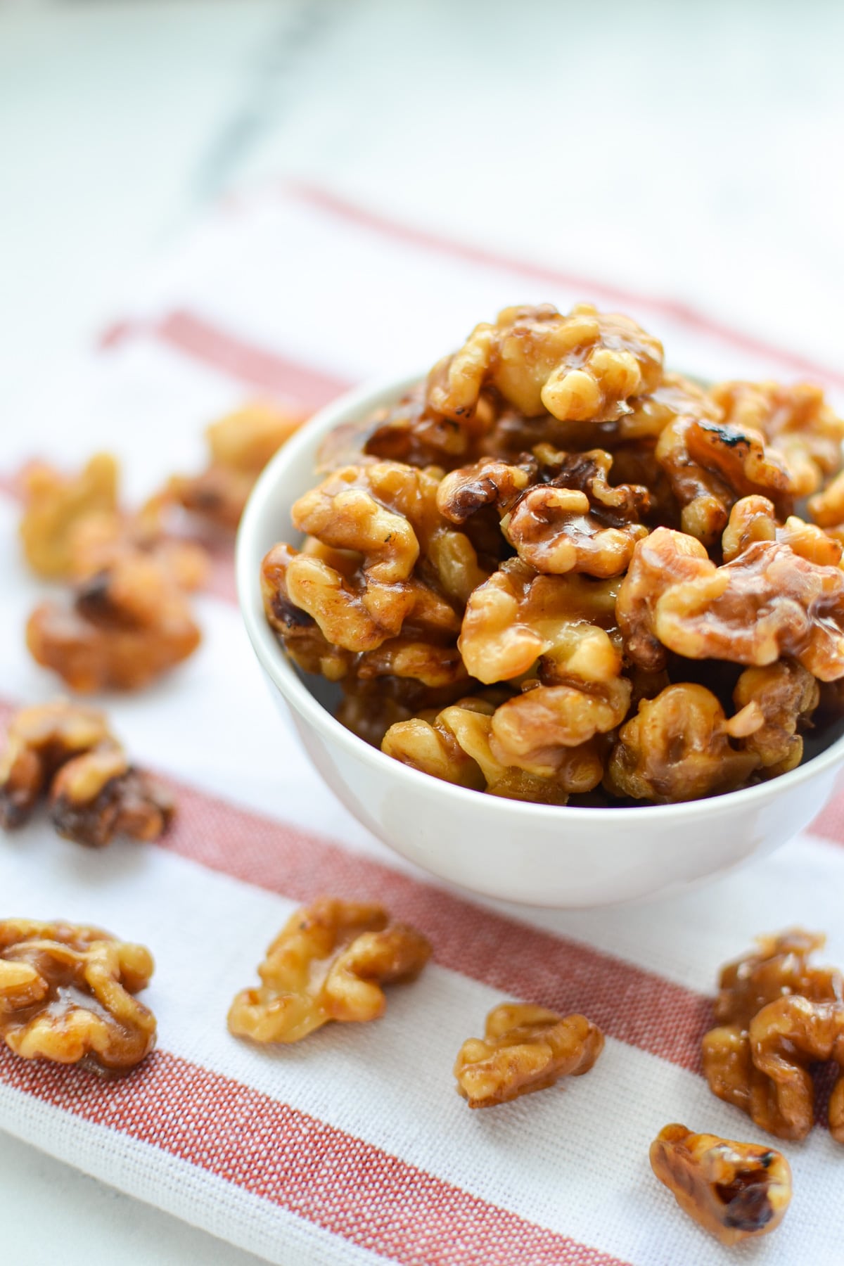 A small white bowl of canded walnuts on a striped napkin.