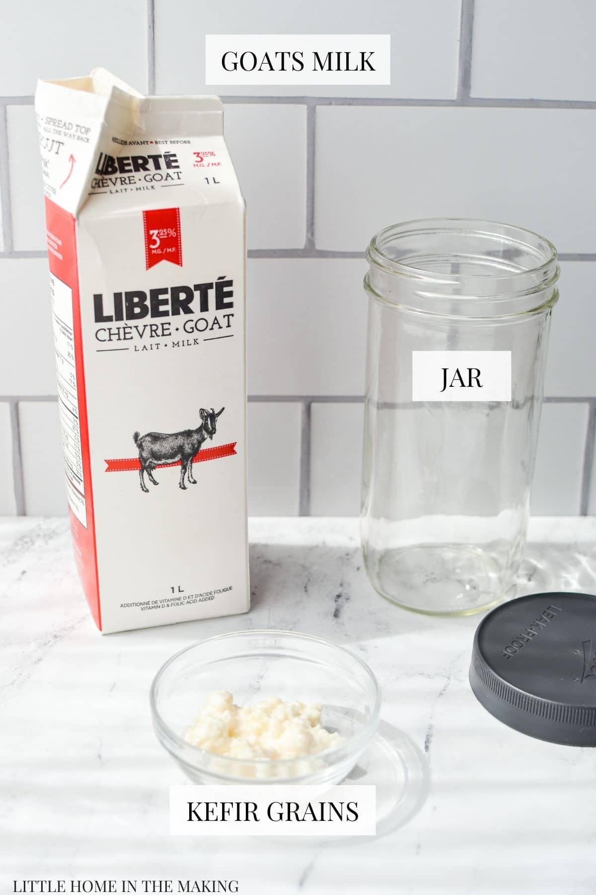 A marble counter with a carton of goats milk, kefir grains, and a clean glass jar.