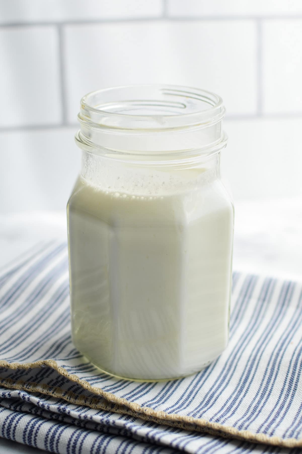 A jar of finished goat's milk kefir on a blue striped napkin.