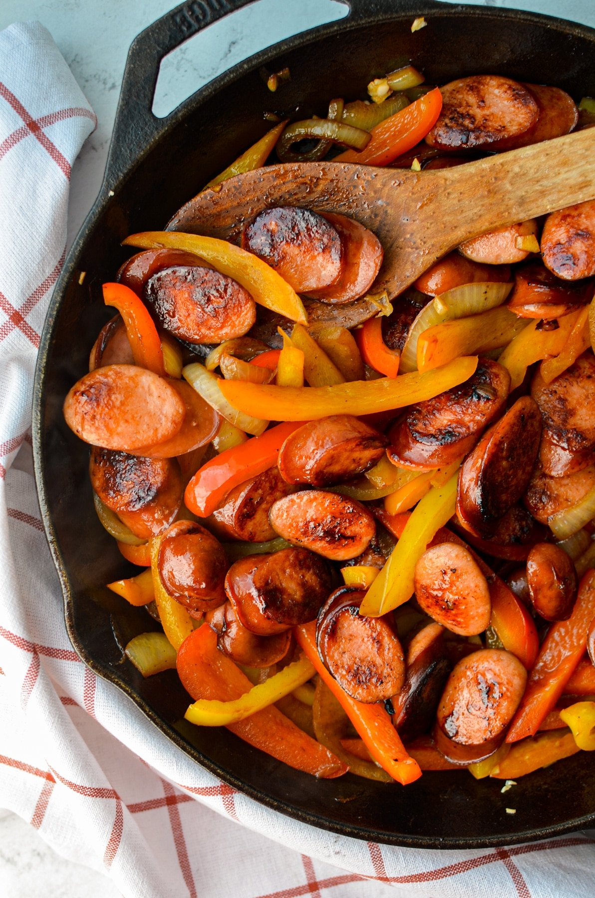 An overhead shot of a skillet with sliced peppers, onions, and sausage.