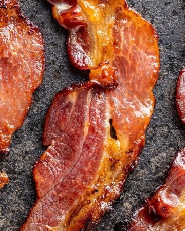 A slice of fully cooked bacon on a dark surface.