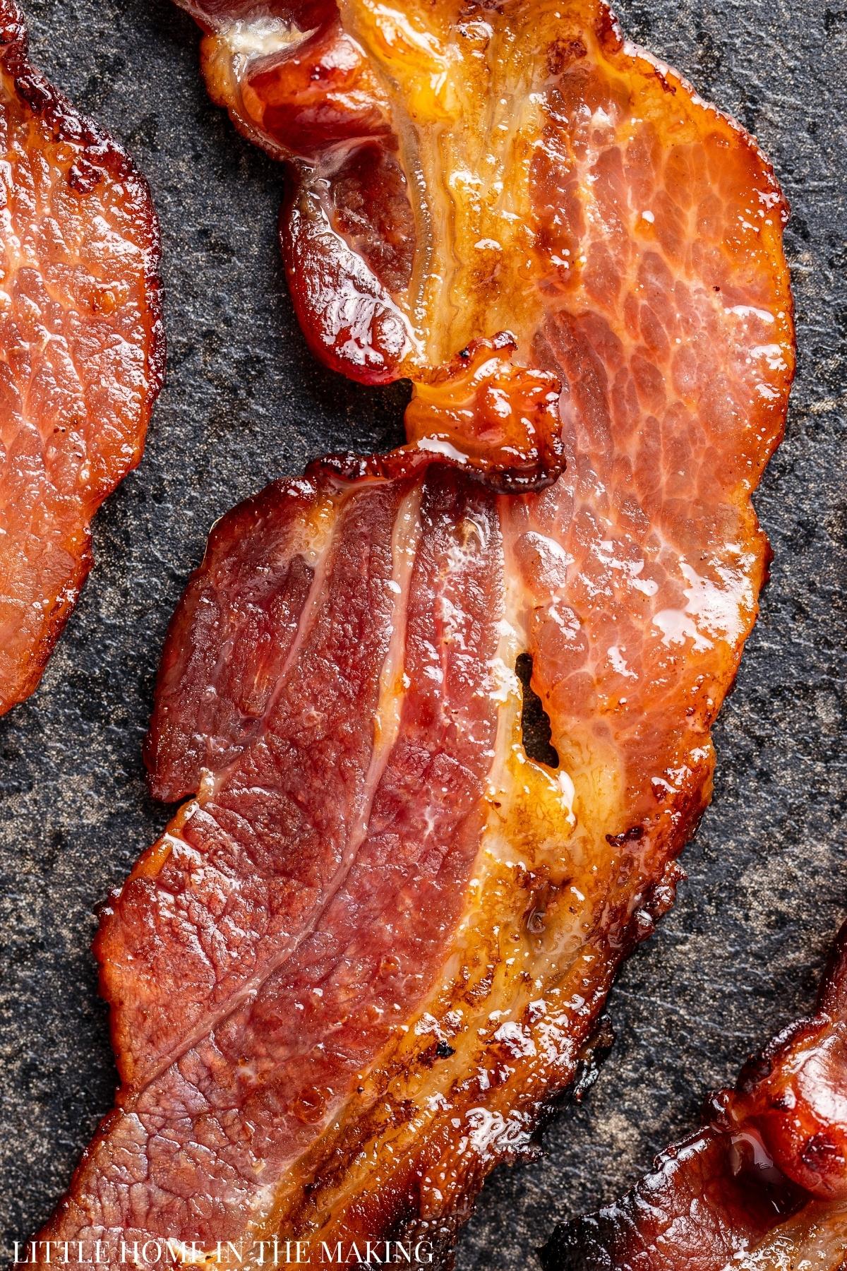 A slice of fully cooked bacon on a dark surface.