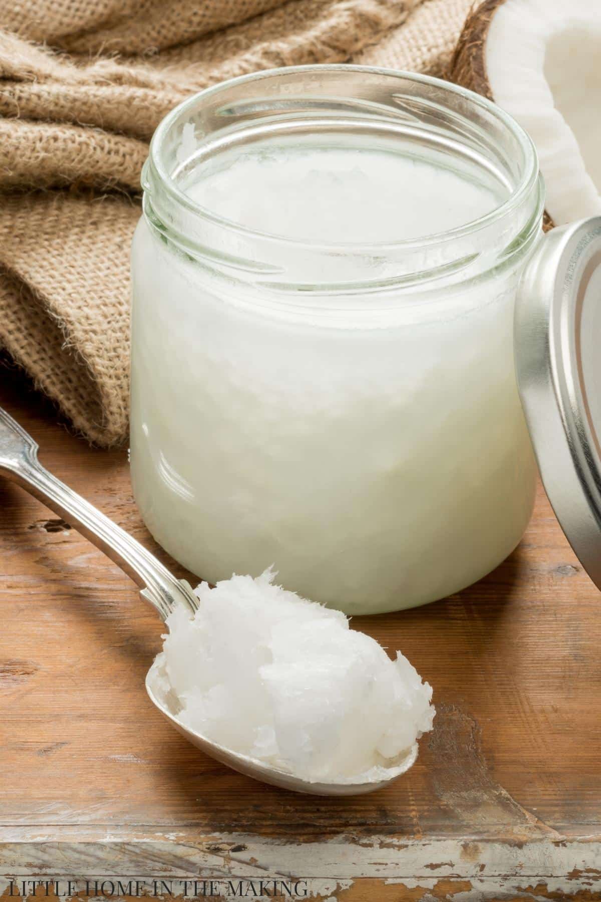 A jar of coconut oil, with a spoon of coconut oil resting on the table.