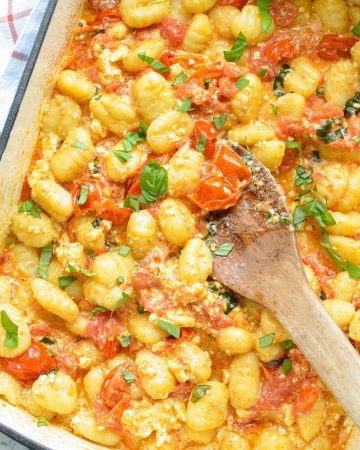 A baking dish with gnocchi pasta, crushed cherry tomatoes, and basil.