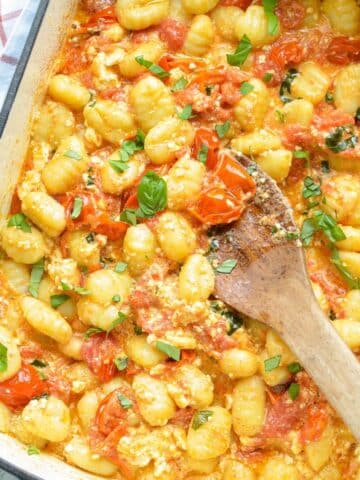 A baking dish with gnocchi pasta, crushed cherry tomatoes, and basil.