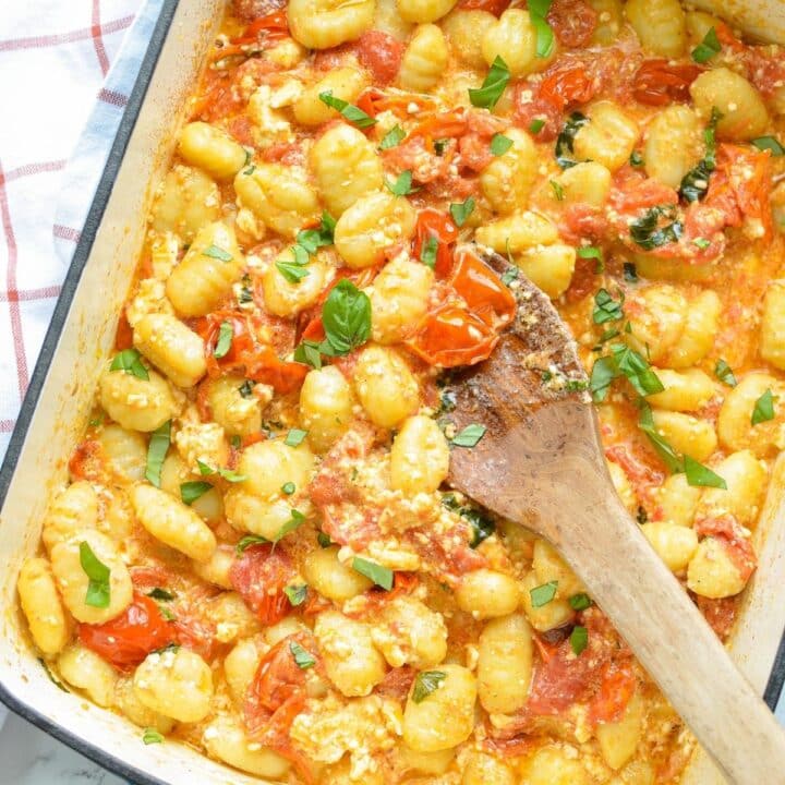 A baking dish with gnocchi pasta, crushed cherry tomatoes, and basil.