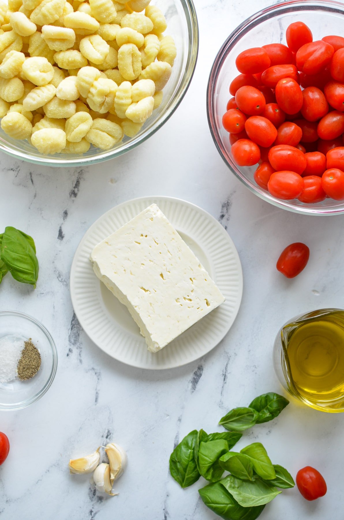The ingredients needed to make baked feta gnocchi: feta, gnocchi, cherry tomatoes, garlic, olive oil, basil, and salt and pepper.