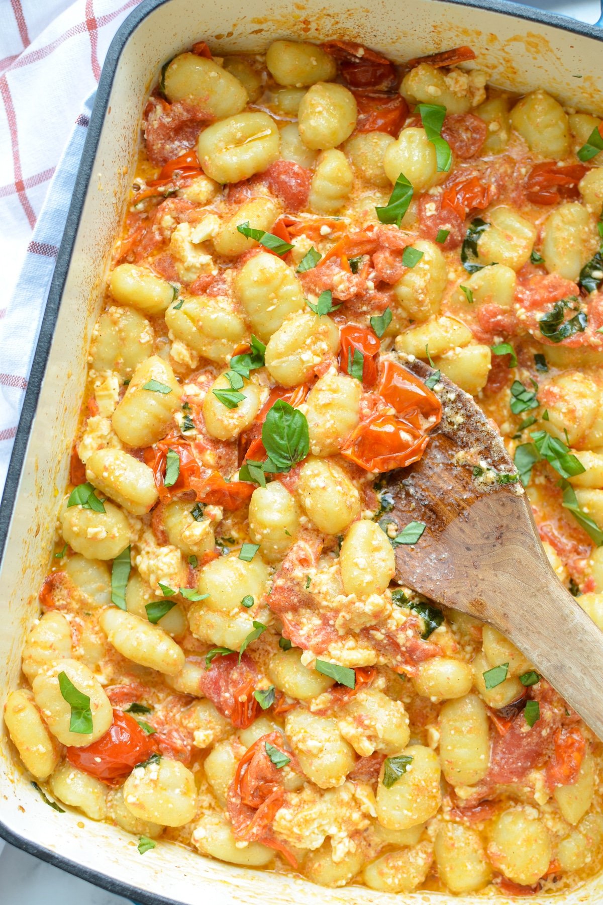 A baking dish with gnocchi pasta, tomatoes, and fresh basil.